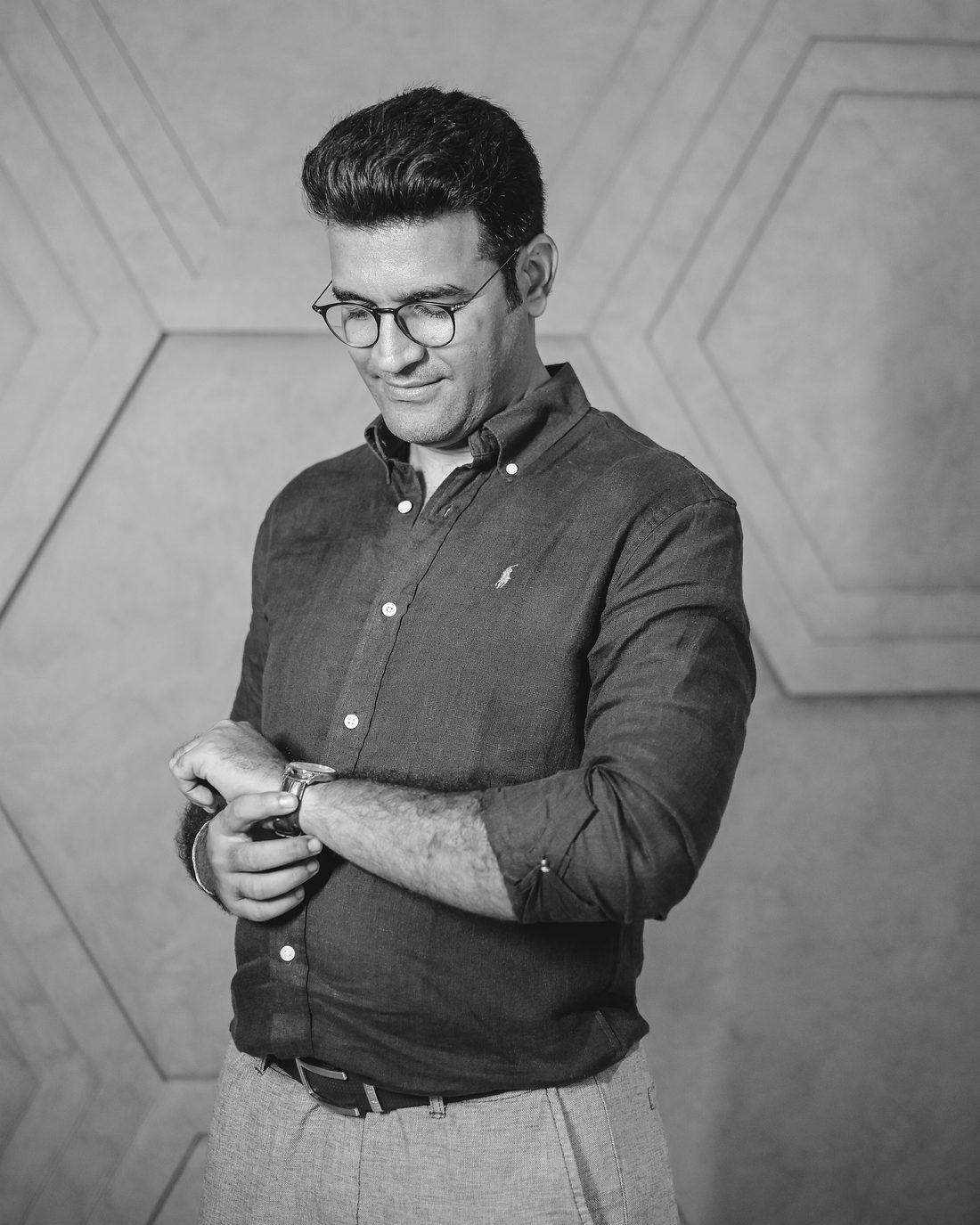 Mehul Dedhia looking down at his watch, patterned wall behind him